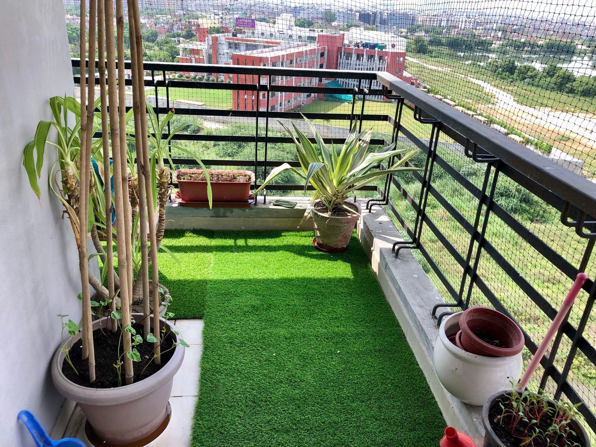 Image of residential balcony, Ghaziabad, India, designed with artificial grass turf and potted plants, pigeon anti-bird netting